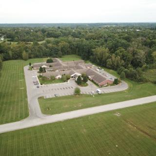 An aerial view of a building surrounded by lush greenery and a spacious parking area.