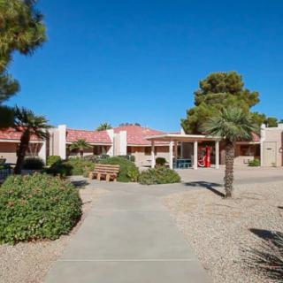 A house with desert landscaping, featuring trees and bushes under a clear blue sky.