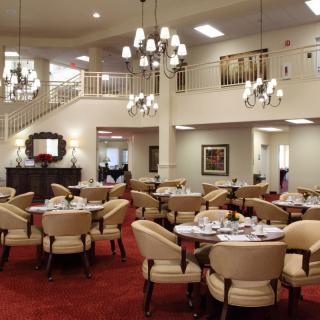 An elegant dining room with multiple tables and chairs, adorned with chandeliers and a red carpet.
