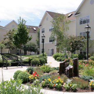 A beautifully landscaped garden with colorful flowers and trees, set in front of a multi-story building.