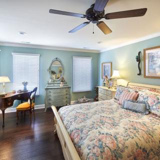 A cozy bedroom with a floral bedspread, elegant furniture, and a ceiling fan.