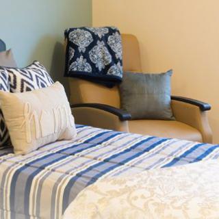 A cozy bedroom featuring a comfortable chair and a neatly made bed with decorative pillows and a striped blanket.