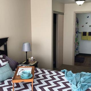A cozy bedroom with a zigzag patterned bedspread, pillows, and a bedside lamp.