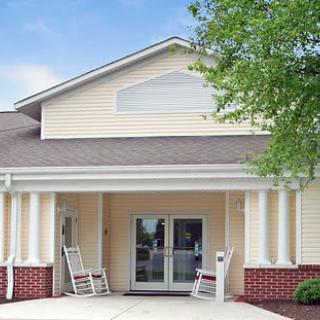 A building entrance with rocking chairs on the porch and columns supporting the roof.