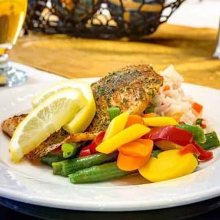 A colorful plate featuring grilled salmon, assorted steamed vegetables, and lemon wedges.