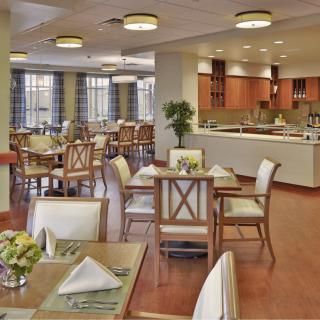 A modern restaurant dining area with neatly arranged tables and chairs, featuring a view of the open kitchen.