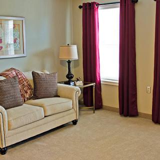 A cozy living room with a beige sofa, decorative pillows, a lamp, and burgundy curtains.
