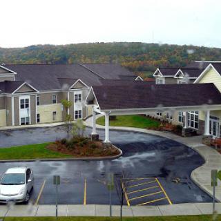 A view of a modern residential building complex surrounded by greenery and a parking area.