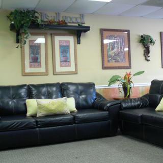 A cozy seating area with black leather couches, decorated with indoor plants and wall art.