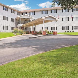A sunny day view of a residential apartment building with a well-maintained lawn and driveway.