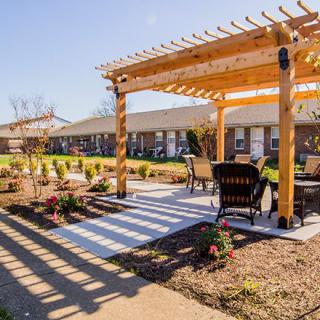A cozy outdoor area featuring a wooden pergola with comfortable seating and a beautifully landscaped garden on a sunny day.
