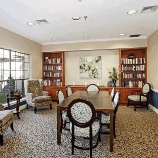A cozy library room with bookshelves, a table, and chairs arranged on a carpeted floor.