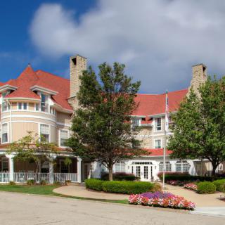 A large, elegant building with a red roof surrounded by trees and landscaping under a partly cloudy sky.