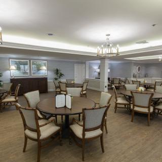 A well-lit dining room with several tables and chairs arranged on a wooden floor.
