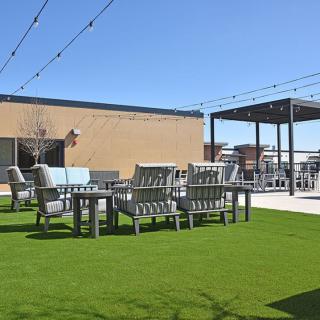 A rooftop patio with seating areas and artificial grass under a clear blue sky.