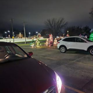 A view of parked cars illuminated by festive holiday lights in a nighttime parking lot.