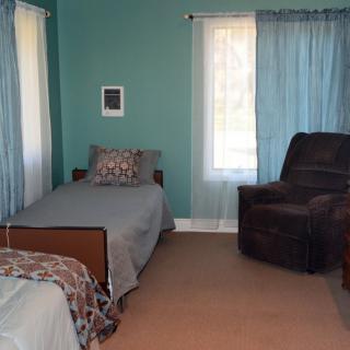 A cozy bedroom with a single bed, armchair, and teal curtains.
