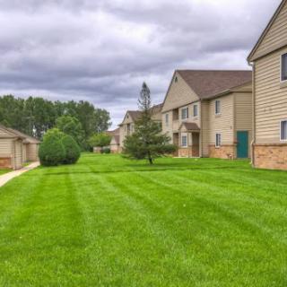 A well-maintained residential area with a lush green lawn and apartment buildings under a cloudy sky.