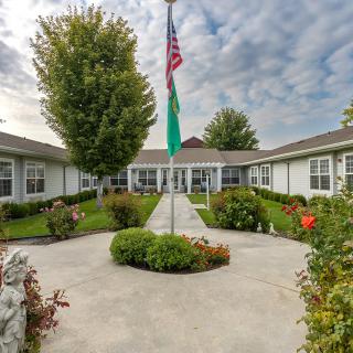 A well-maintained courtyard with a central pathway leading to a building, featuring an American flag and manicured gardens.