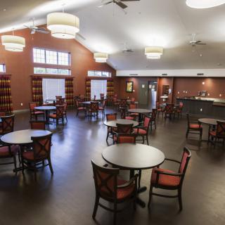 A spacious library room with tables and chairs arranged neatly under warm lighting.
