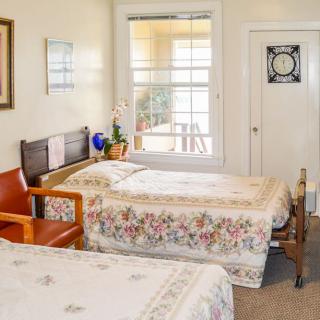 A cozy bedroom with two twin beds featuring floral bedding, a wooden bench, and a large window.