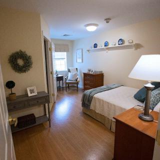 A cozy and well-decorated bedroom featuring a bed, lamp, and a wall shelf with decor.