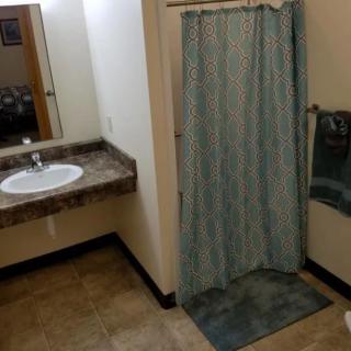 A bathroom with a sink, shower, and towels on a tile floor.