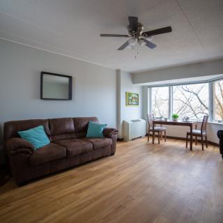 A cozy living room with a brown sofa, wooden floor, and natural light streaming in through a large window.