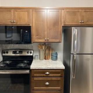A modern kitchen setup with wooden cabinetry, stainless steel appliances including a stove and refrigerator, and various cooking utensils on the countertop.