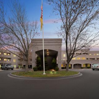 An elegant building entrance with a flagpole and surrounding trees at dusk.