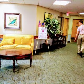 A well-lit lobby area featuring a yellow couch, decorative artwork, and a person walking down the hallway.