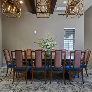 A sophisticated dining room with an elegant table and chairs, adorned with chandeliers and a central flower arrangement.