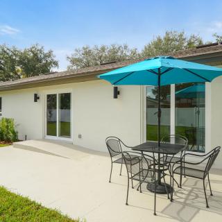 An inviting outdoor patio area with a table, chairs, and a bright blue umbrella beside a modern house.