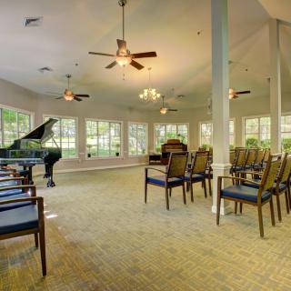 A spacious room with a grand piano, arranged chairs, large windows, and ceiling fans.