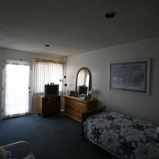 A cozy bedroom with a bed, dresser, mirror, and TV near a window with curtains.