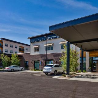 A modern commercial building with a parking lot and cars under a clear blue sky.