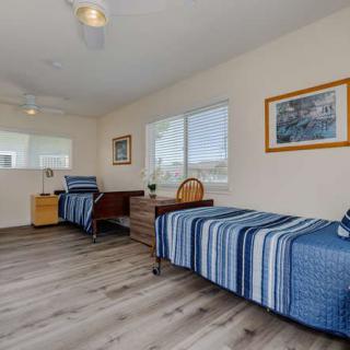 A bright and airy bedroom with a single bed featuring blue striped bedding, a desk and chair, large windows, and artwork on the walls.