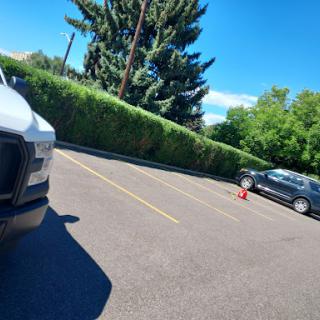 A view of a parking lot with two vehicles and lush greenery under a clear blue sky.