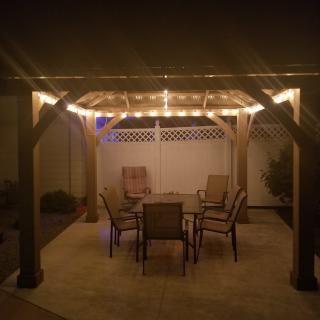 An inviting outdoor patio setup with a pergola, illuminated by string lights and furnished with a dining table and chairs.