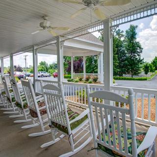 A row of white rocking chairs on a covered porch overlooking a suburban street.