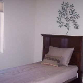A minimalist bedroom featuring a single bed with a wooden headboard and decorative wall decal.