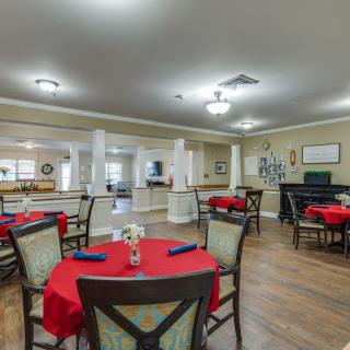 A spacious dining room with tables covered in red tablecloths and neatly arranged chairs.