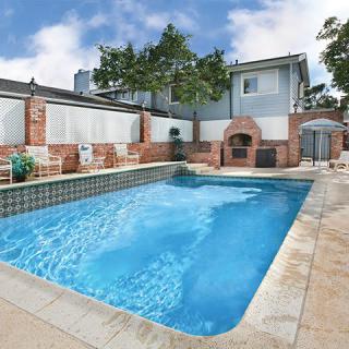 A residential backyard featuring a clear blue swimming pool and patio area.