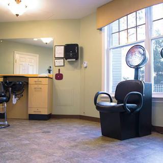A clean and brightly lit hair salon with a salon chair and hair dryer near a large window.
