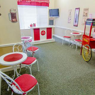 A retro-themed candy shop with red and white decor, featuring tables, chairs, and a popcorn machine.