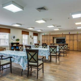 A well-lit dining area with multiple tables and chairs, featuring wooden flooring and large windows.
