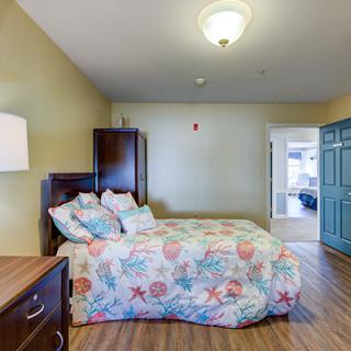 A well-lit bedroom with a colorful bedspread and wooden flooring.