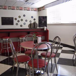 A retro-style diner interior featuring red chairs, round tables, and a classic checkered floor.