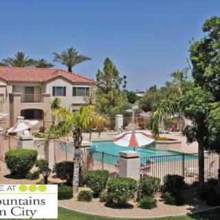 A scenic view of an apartment complex featuring a swimming pool surrounded by vibrant landscaping and palm trees.