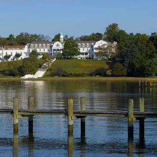A grand mansion overlooking a serene lake with a wooden pier in the foreground.